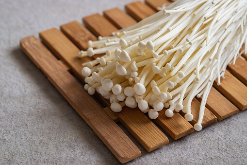 White enoki mushrooms lying on a wooden board