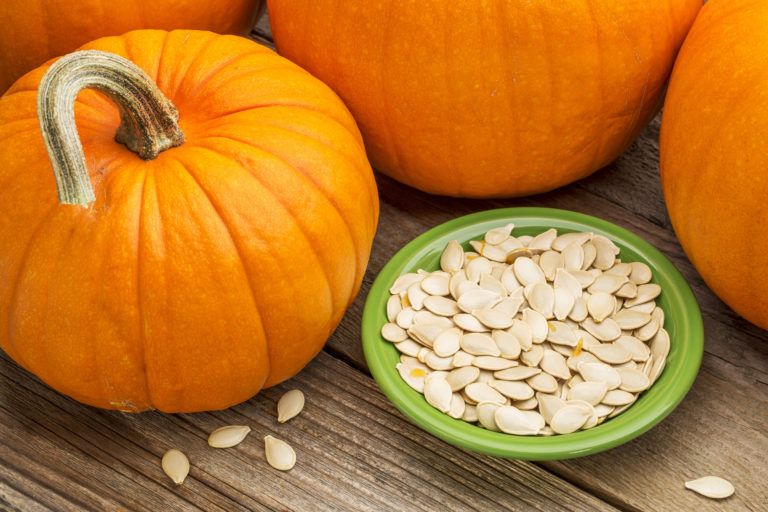 Small pumpkins in table with pumpkin seeds in a bowl next to them