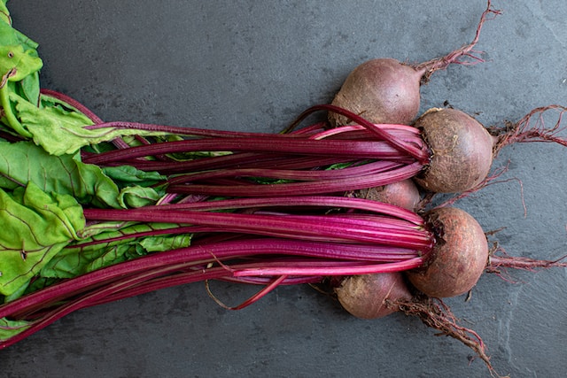 A bunch of freshly picked beetroot with leaves and steams intact, lying on a table